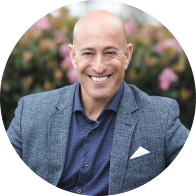 head and shoulders shot of a man standing outside in front of flowers in a light blue suit jacket and dark blue shirt